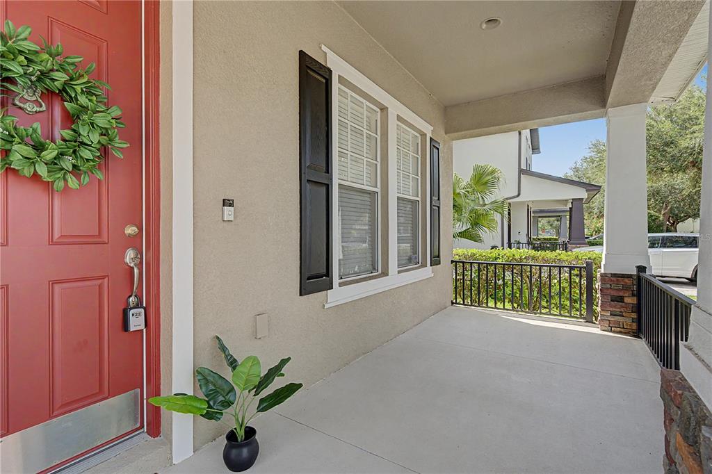 A covered front porch features a red door, a potted plant, and black metal railings — 8152 LAGERFELD DRIVE, LAND O LAKES, FL