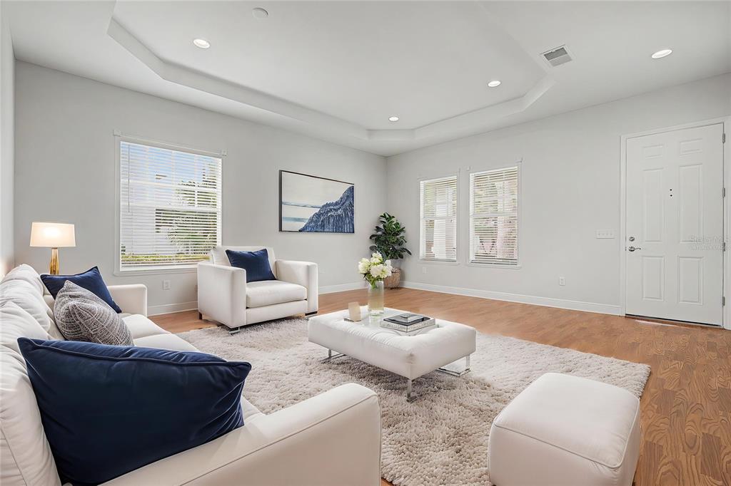 A bright living room features white furniture, a plush rug, and a tray ceiling — 8152 LAGERFELD DRIVE, LAND O LAKES, FL