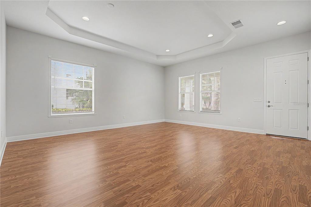 An empty room features light gray walls, wood-look flooring, a tray ceiling, and three windows — 8152 LAGERFELD DRIVE, LAND O LAKES, FL