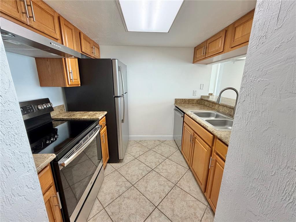 A galley kitchen features oak cabinets, granite countertops, stainless steel appliances, and tile flooring — 3600 S OCEAN SHORE BOULEVARD UNIT 812, FLAGLER BEACH, FL