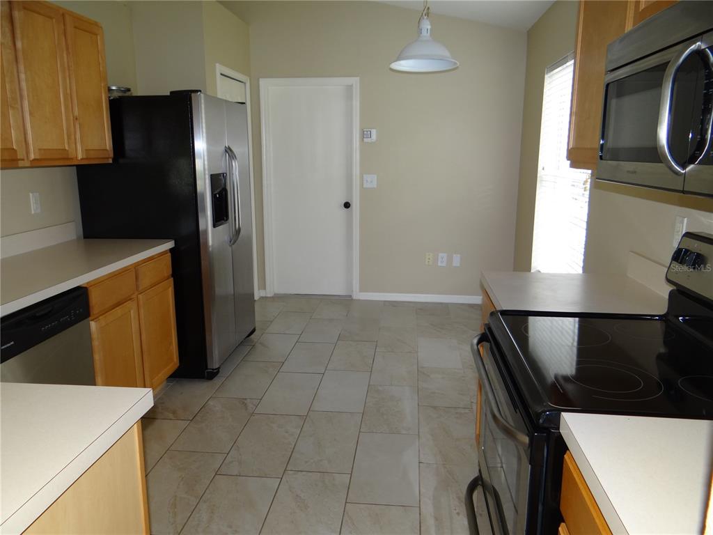 A kitchen features light wood cabinets, stainless steel appliances, and tan tile flooring — 5930 WAR ADMIRAL DRIVE, WESLEY CHAPEL, FL