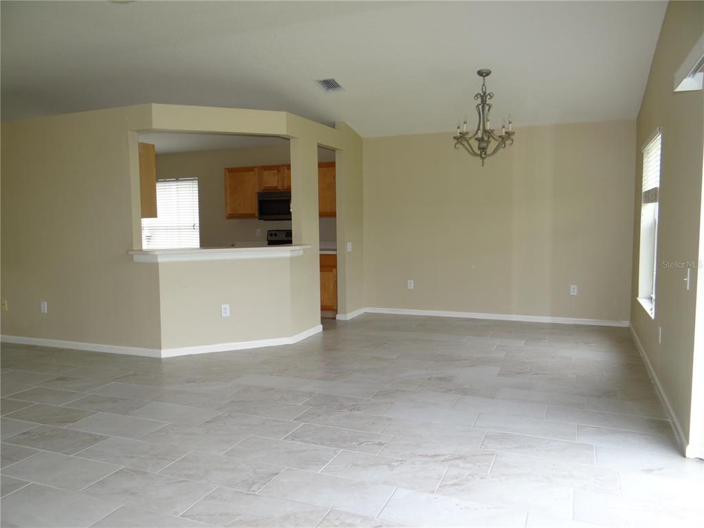 An open-concept dining area features beige walls, tile flooring, and a chandelier — 5930 WAR ADMIRAL DRIVE, WESLEY CHAPEL, FL