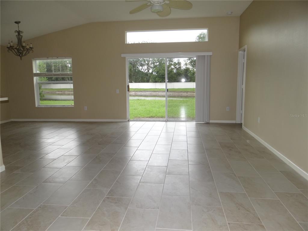 A living room with beige walls, tile flooring, a ceiling fan, and sliding glass doors — 5930 WAR ADMIRAL DRIVE, WESLEY CHAPEL, FL