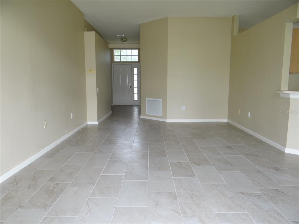 An empty room with light-colored tile flooring and beige walls leads to a front door — 5930 WAR ADMIRAL DRIVE, WESLEY CHAPEL, FL