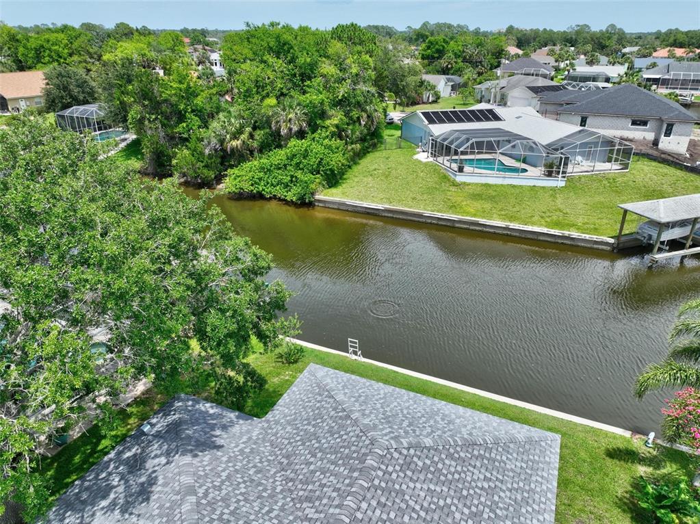 An aerial view shows a house with a shingled roof overlooking a canal and pool — 56 COLUMBIA LANE, PALM COAST, FL