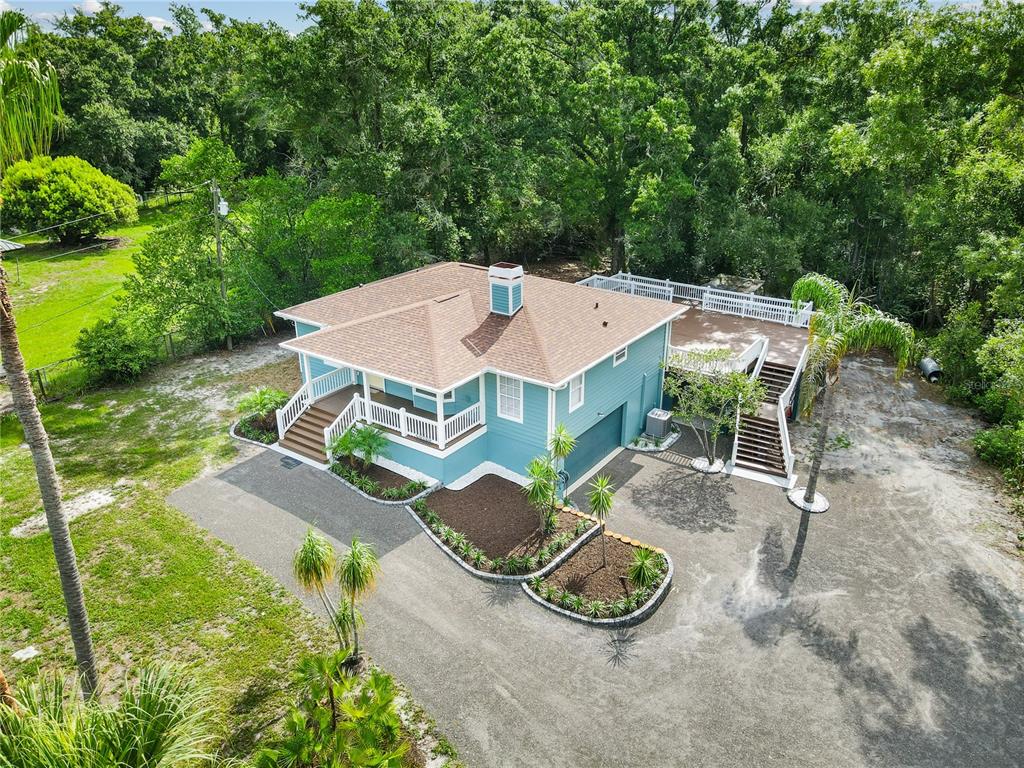 An aerial view of a blue house with a brown roof, wraparound porch, and deck — 2650 20 MILE LEVEL ROAD, LAND O LAKES, FL