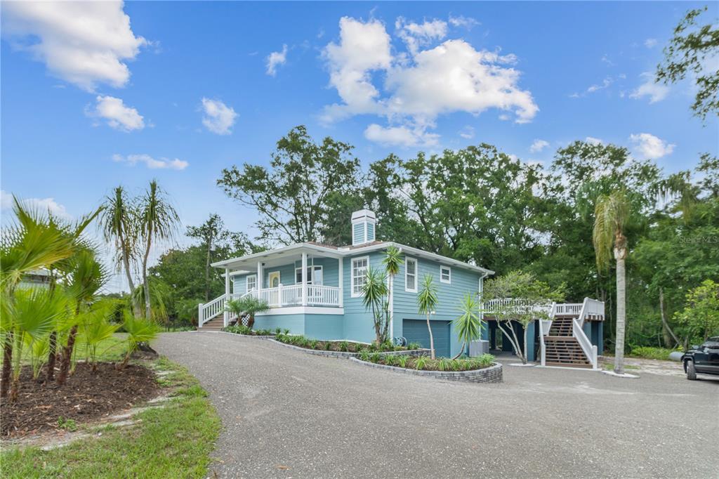A blue elevated house with a wrap-around porch, a garage, and a long gravel driveway — 2650 20 MILE LEVEL ROAD, LAND O LAKES, FL