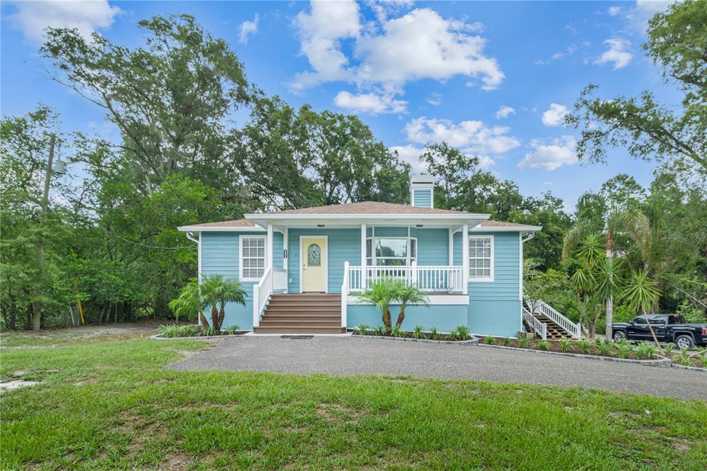 A light blue house with a front porch, stairs, and a driveway sits on a lawn — 2650 20 MILE LEVEL ROAD, LAND O LAKES, FL