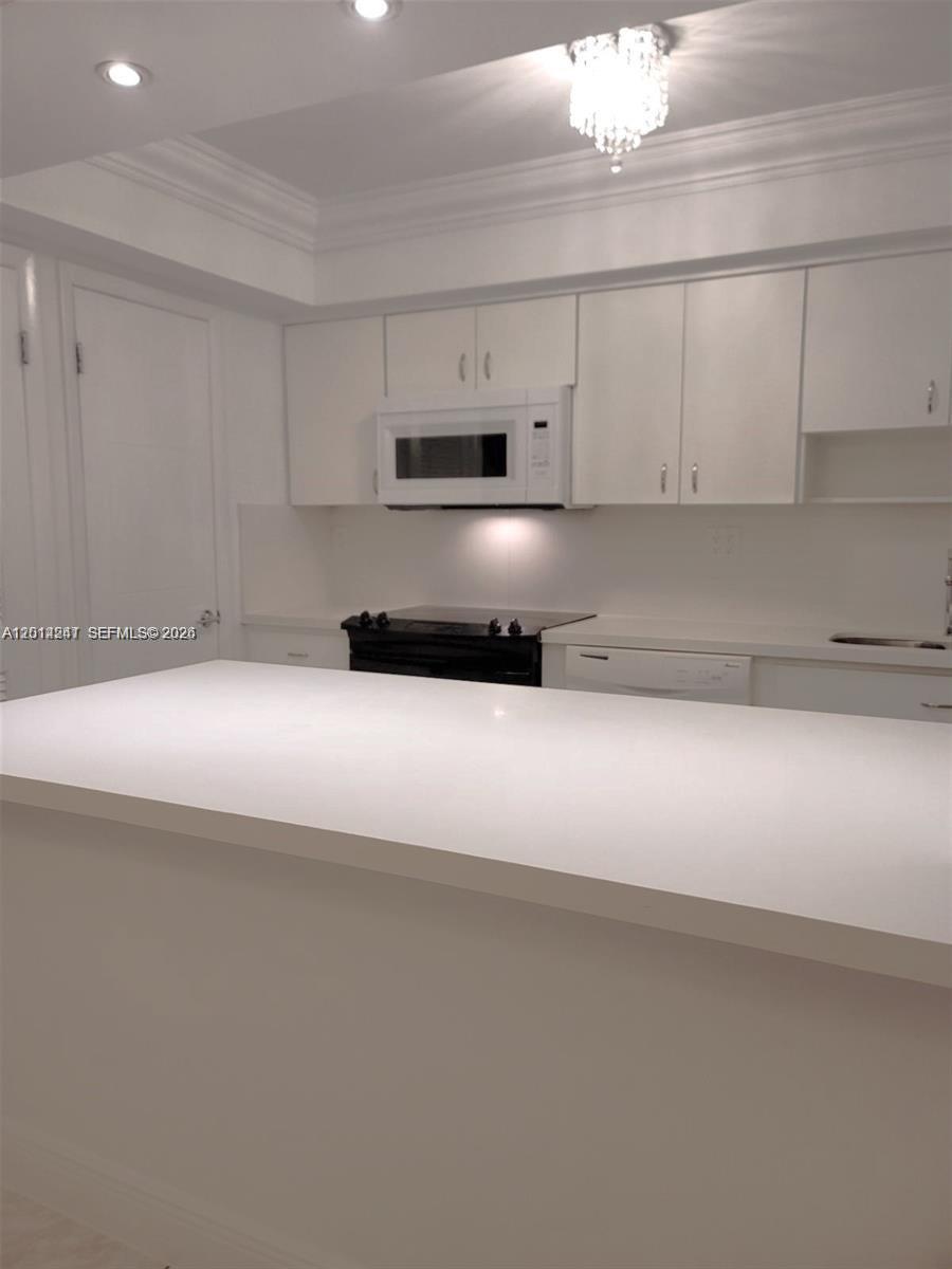 A kitchen features white cabinets, a white countertop island, and a black stove — 8401 SW 107 AVE # 260E, Miami FL 33173, MIAMI, FL