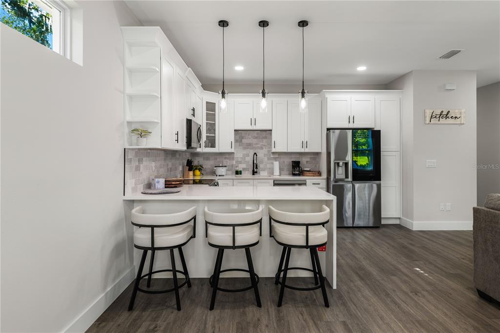A modern kitchen features white cabinetry, a quartz island with three barstools, and stainless appliances — 192-194 S LEMON AVENUE, BROOKSVILLE, FL