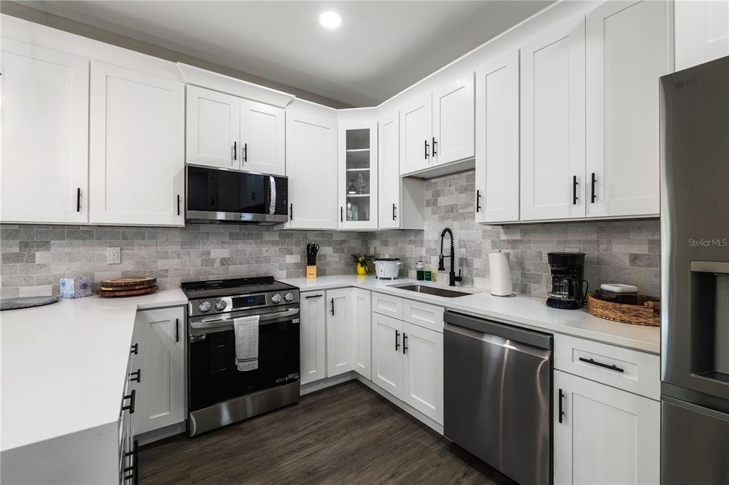 A modern kitchen features white cabinets, stainless steel appliances, and a gray tiled backsplash — 192-194 S LEMON AVENUE, BROOKSVILLE, FL
