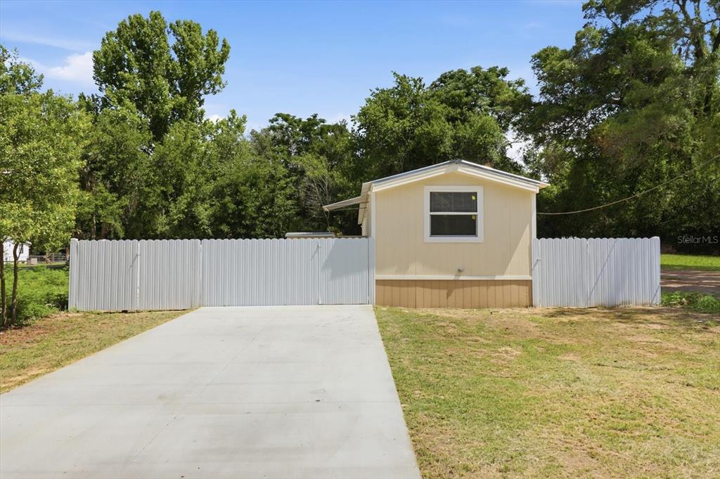 A small, light-colored mobile home sits behind a white metal fence with a concrete driveway — 6403 W TANGERINE LANE, CRYSTAL RIVER, FL