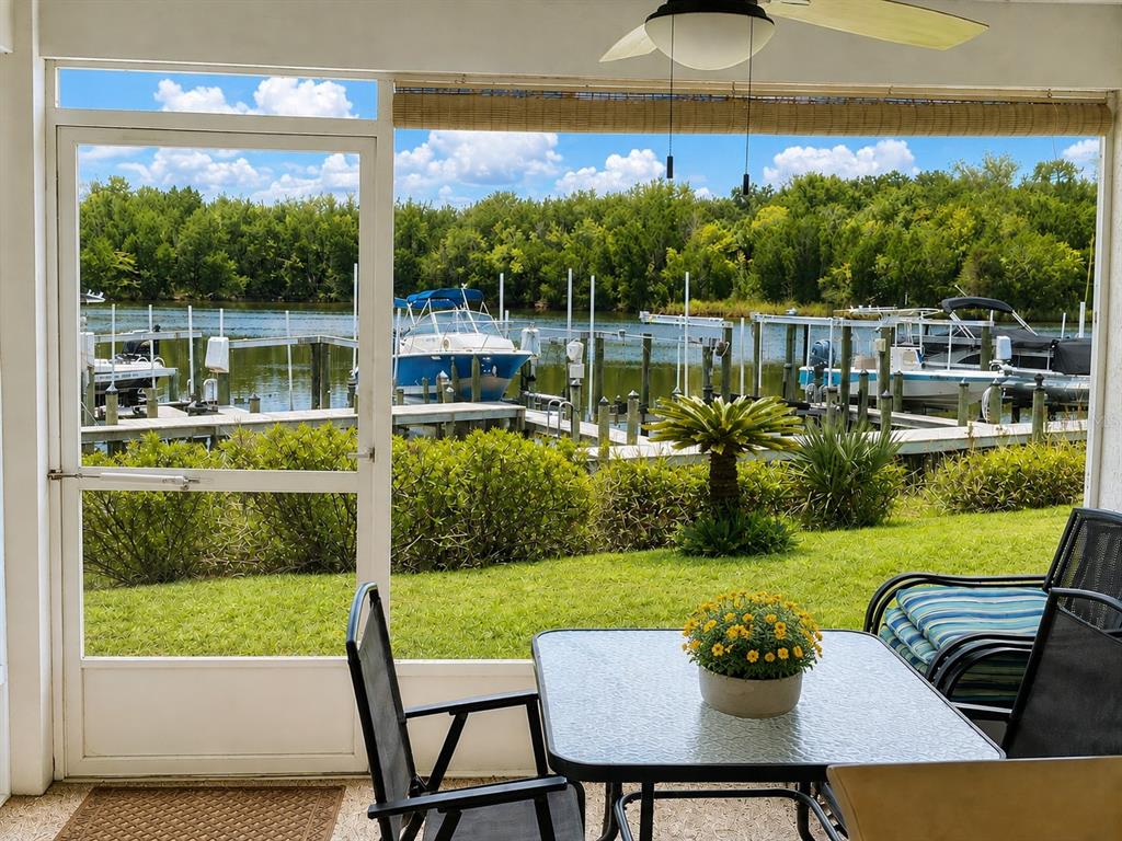 A screened-in patio features a dining set overlooking a grassy lawn, boat docks, and water — 11122 W COVE HARBOR DRIVE UNIT 112, CRYSTAL RIVER, FL