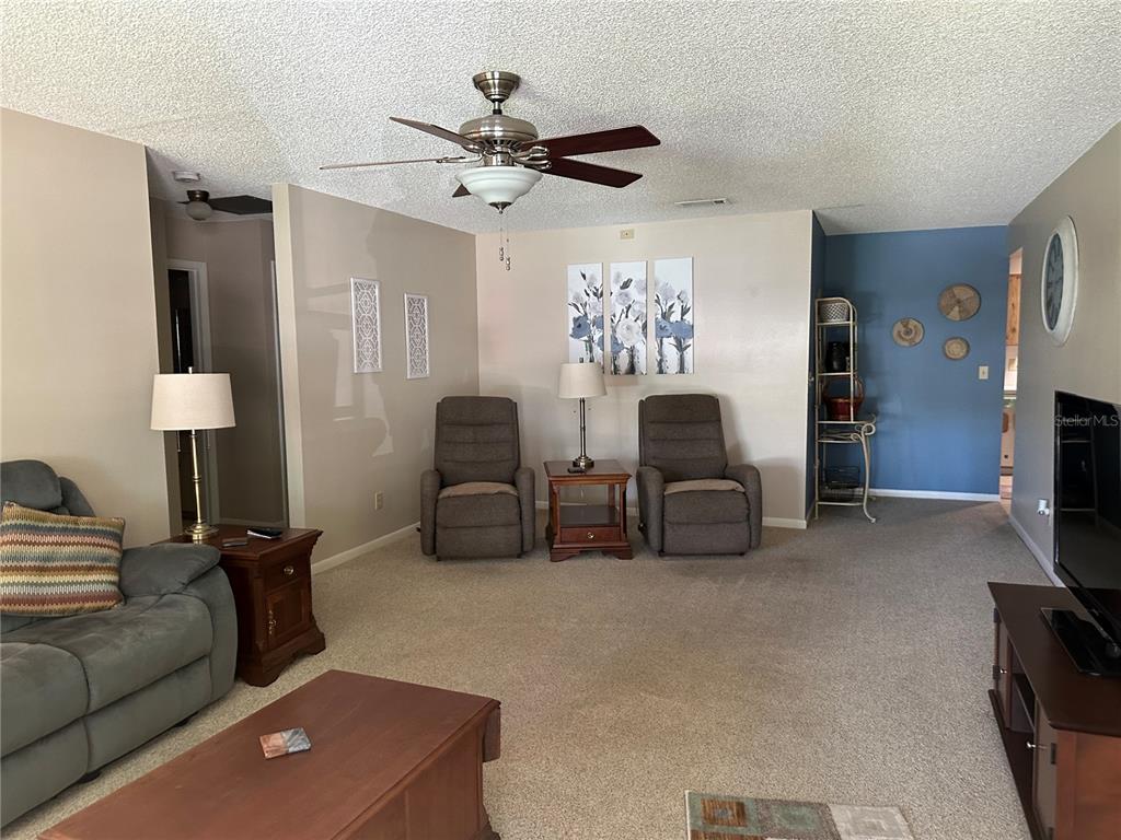 A living room features a ceiling fan, carpeted floors, two recliners, and a blue accent wall — 8680 SW 94TH LANE UNIT G, OCALA, FL