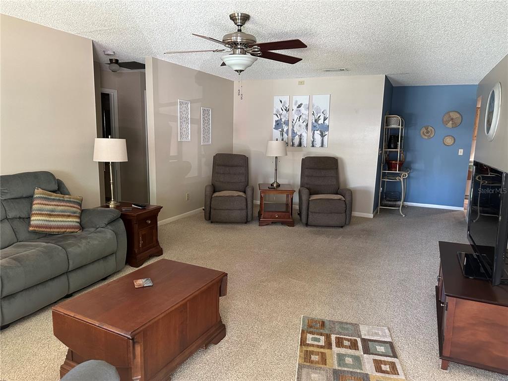 A living room features carpeted flooring, a ceiling fan, a sofa, two recliners, and a television — 8680 SW 94TH LANE UNIT G, OCALA, FL