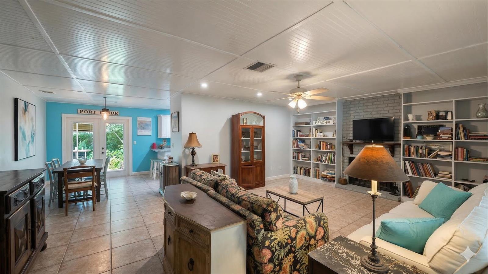 A living room and dining area with tile floors, built-in bookshelves, and a brick fireplace — 5679 Sims Road, Delray Beach FL 33484, DELRAY BEACH, FL