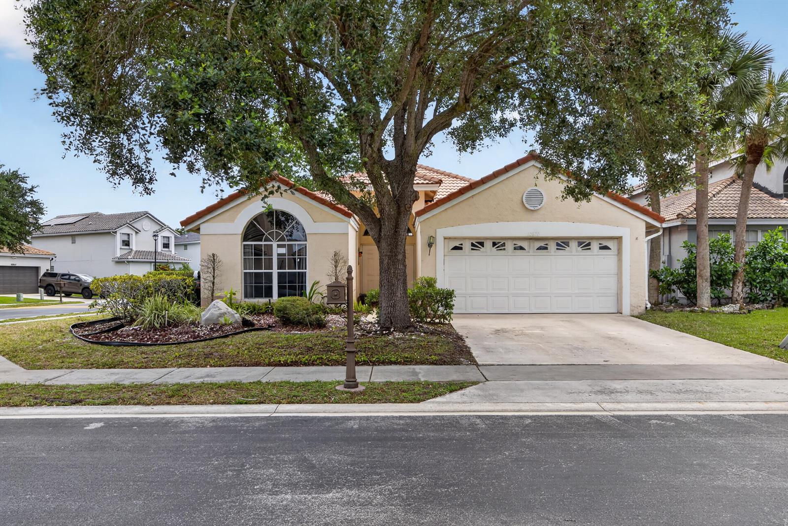 A single-story house with a beige stucco exterior, a two-car garage, and a large tree — 10870 Old Bridgeport Lane, Boca Raton FL 33498, BOCA RATON, FL