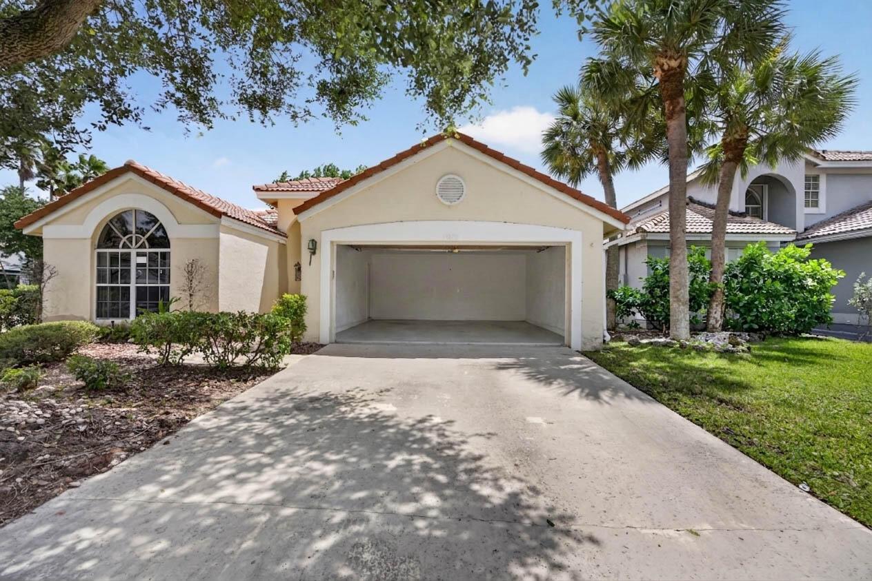 A beige house exterior with a concrete driveway and an open two-car garage — 10870 Old Bridgeport Lane, Boca Raton FL 33498, BOCA RATON, FL