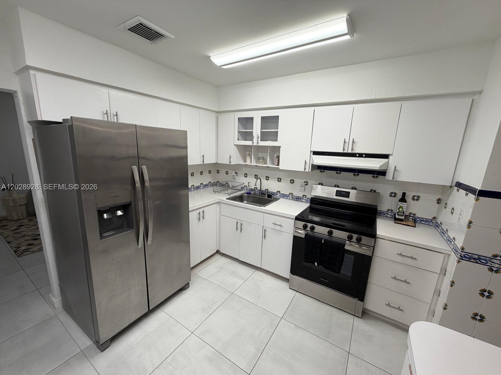 A kitchen features white cabinets, stainless steel appliances, a tiled backsplash, and light-colored floor tiles — 3600 SW 26th St, Miami FL 33133, MIAMI, FL