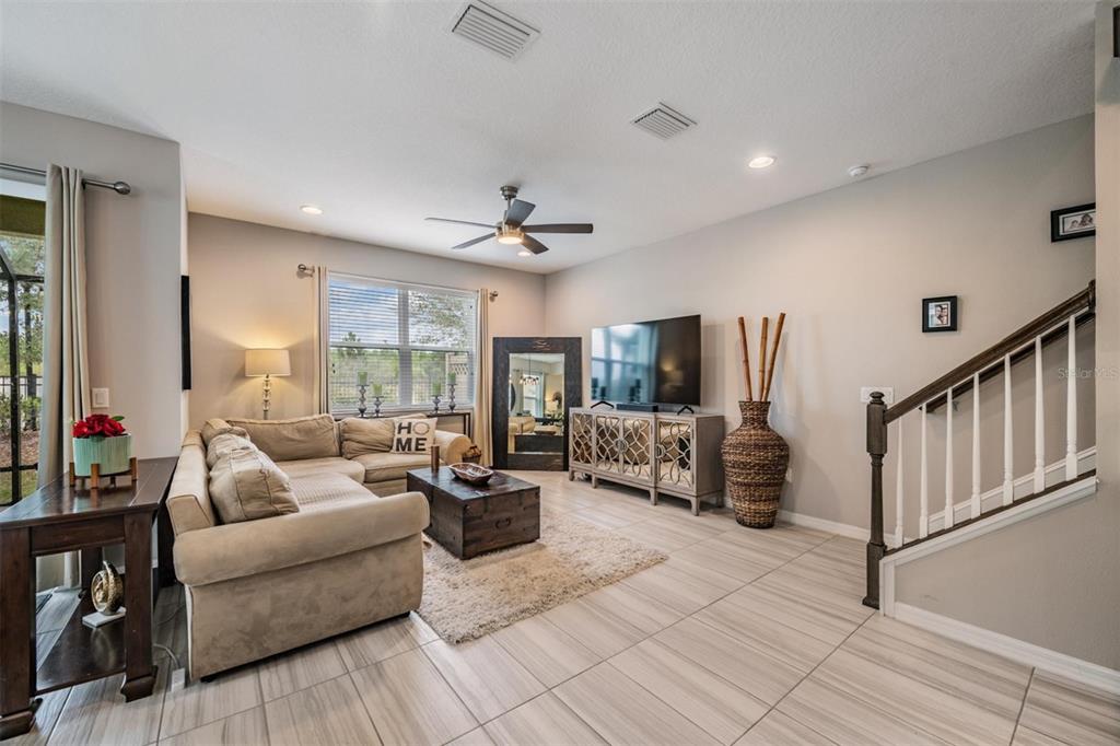 A living room features a beige sectional sofa, a television console, and a staircase — 29947 SOUTHWELL LANE, WESLEY CHAPEL, FL