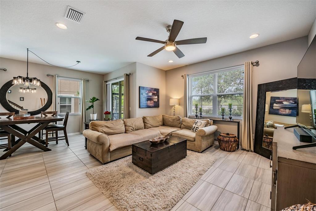 A living room with tile floors, a sectional sofa, a wooden coffee table, and dining area — 29947 SOUTHWELL LANE, WESLEY CHAPEL, FL