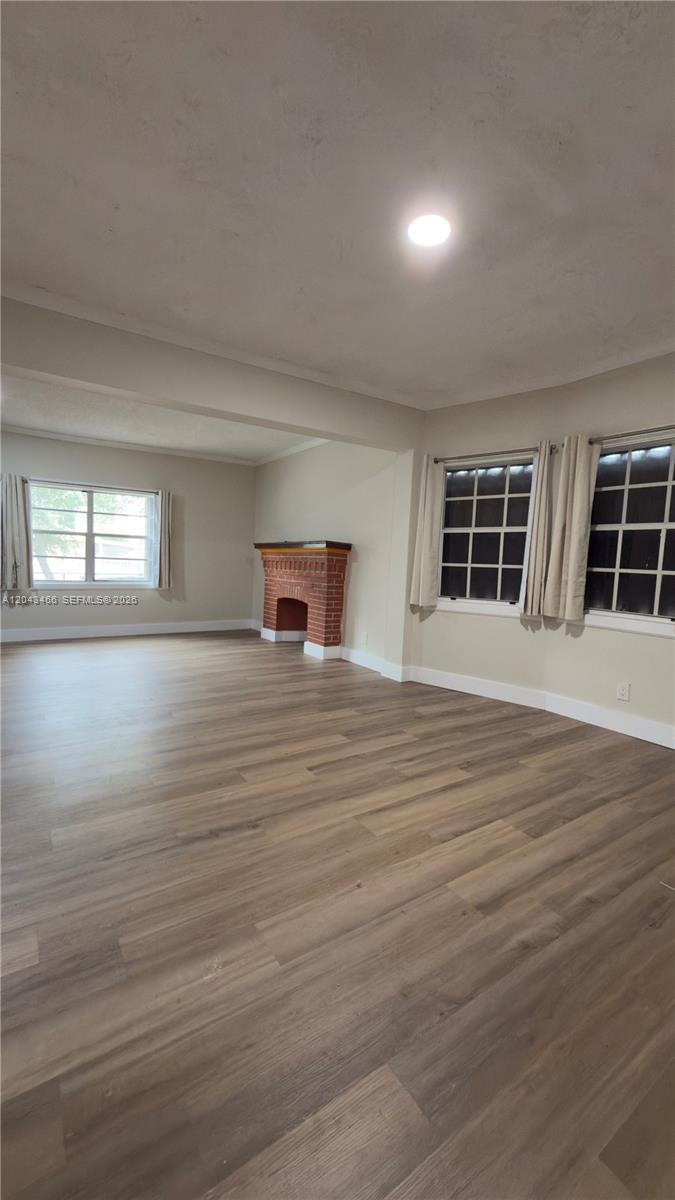 An empty living room features light wood-look flooring, beige walls, and a brick fireplace — 103 NW 35th St, Miami FL 33127, MIAMI, FL