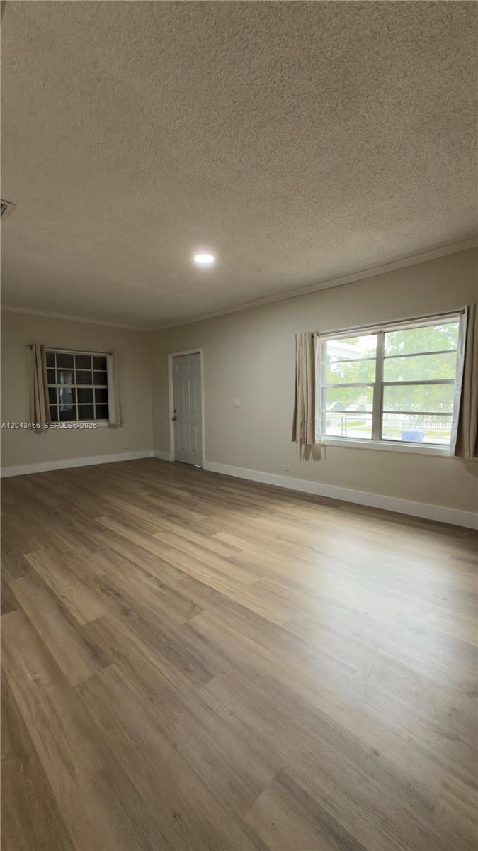 An empty living room features light wood-look flooring, beige walls, and two windows with curtains — 103 NW 35th St, Miami FL 33127, MIAMI, FL