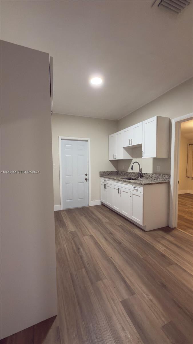 A kitchen features white cabinets, granite countertops, and wood-look flooring — 103 NW 35th St, Miami FL 33127, MIAMI, FL