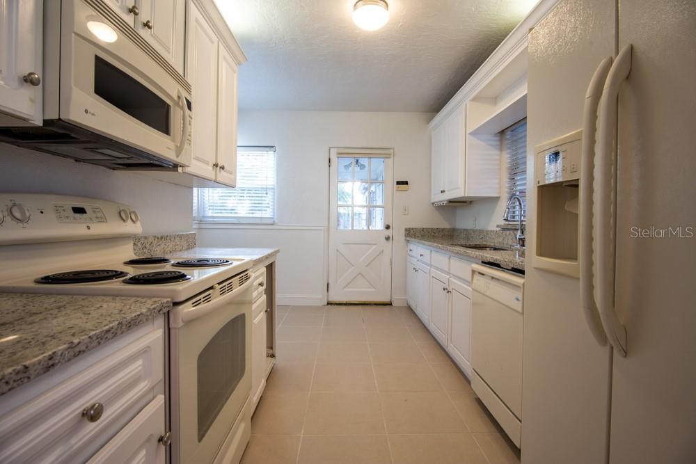 A kitchen features white cabinets, granite countertops, white appliances, and a door to the outside — 1840 BAYLARIAN BOULEVARD, ORLANDO, FL