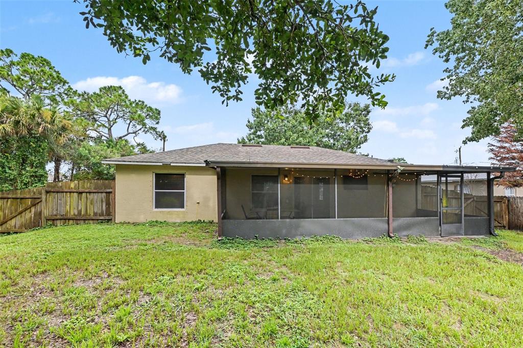 A backyard view of a single-story house with a screened-in porch and a wooden fence — 6289 LEONARD AVENUE, COCOA, FL