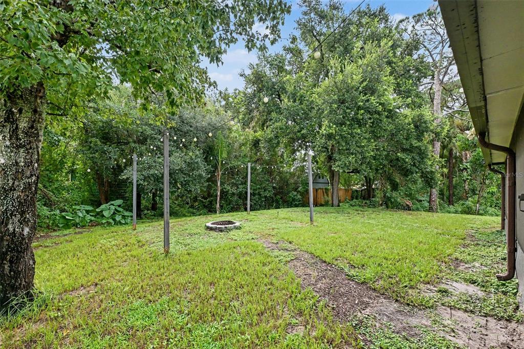 A grassy backyard features a fire pit, string lights on poles, and surrounding mature trees — 6289 LEONARD AVENUE, COCOA, FL