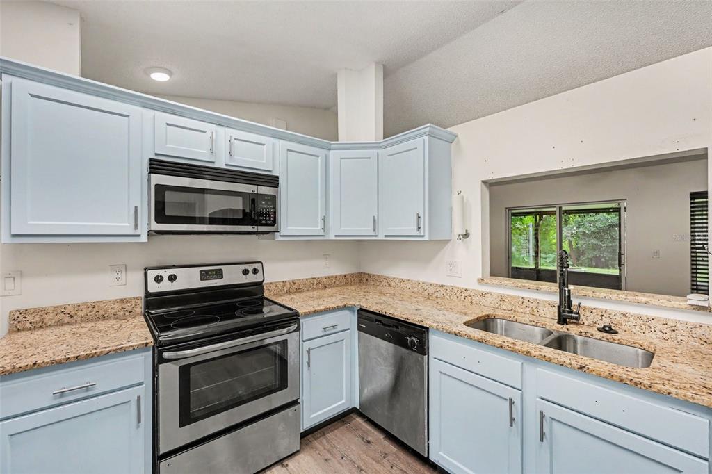 A kitchen features light blue cabinets, granite countertops, stainless steel appliances, and a pass-through window — 6289 LEONARD AVENUE, COCOA, FL