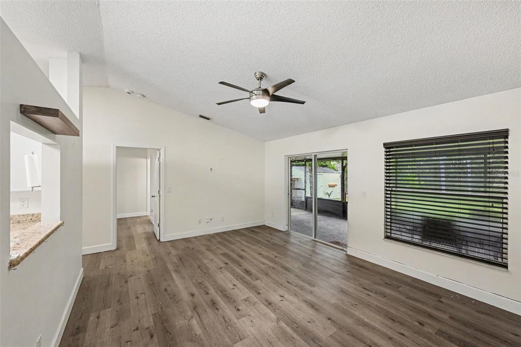 An empty living room with wood-look flooring, a vaulted ceiling, ceiling fan, and sliding glass doors — 6289 LEONARD AVENUE, COCOA, FL