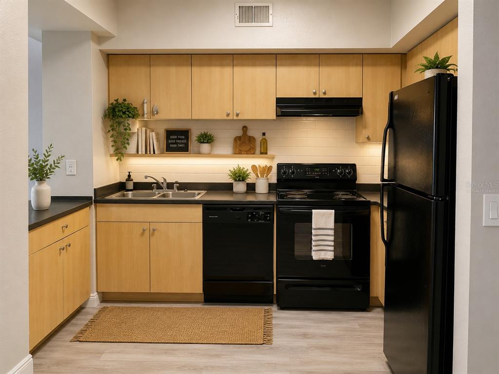 A kitchen features light wood cabinets, black appliances, a black countertop, and a jute rug — 520 S ARMENIA AVENUE UNIT 1235, TAMPA, FL