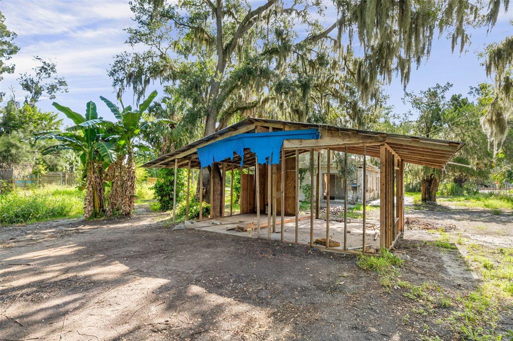 An open-sided wooden frame structure stands in a yard with trees and a banana plant — 3415 41ST STREET E, PALMETTO, FL