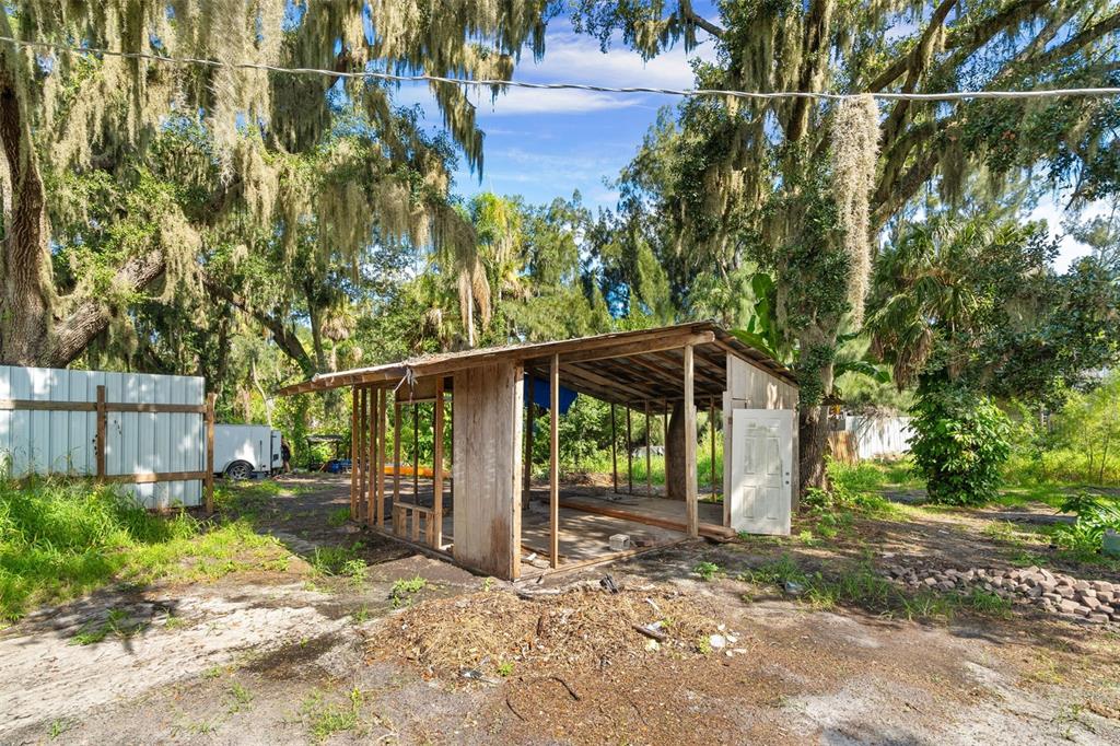 An open-sided wooden shed stands in a grassy yard under large, moss-draped oak trees — 3415 41ST STREET E, PALMETTO, FL