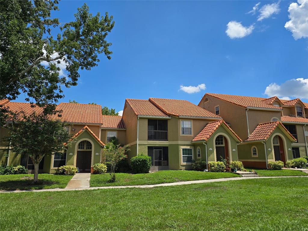 A row of two-story townhouses features tan stucco walls, orange tile roofs, and arched entryways — 409 FOUNTAINHEAD CIRCLE, KISSIMMEE, FL