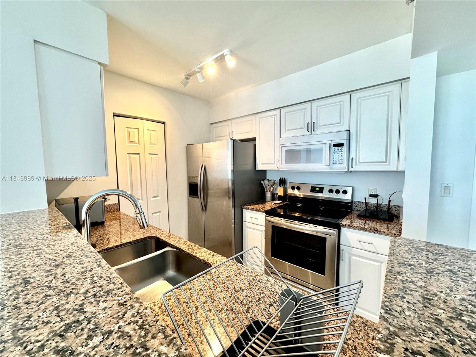 A kitchen features stainless steel appliances, white cabinets, and speckled granite countertops — 1155 Brickell Bay Dr # 906, Miami FL 33131, MIAMI, FL