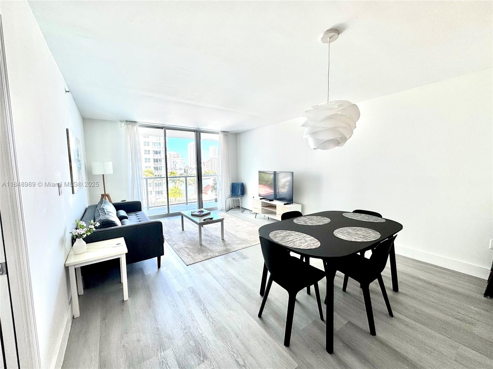 A living and dining area features light wood-look flooring, white walls, and a balcony view — 1155 Brickell Bay Dr # 906, Miami FL 33131, MIAMI, FL