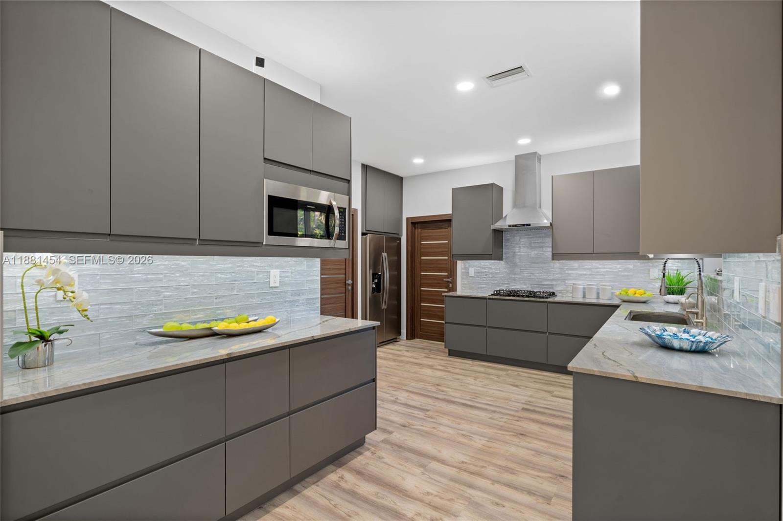 A modern kitchen features gray flat-panel cabinets, stainless steel appliances, and light-colored stone countertops — 1155 Tyler St, Hollywood FL 33019, HOLLYWOOD, FL