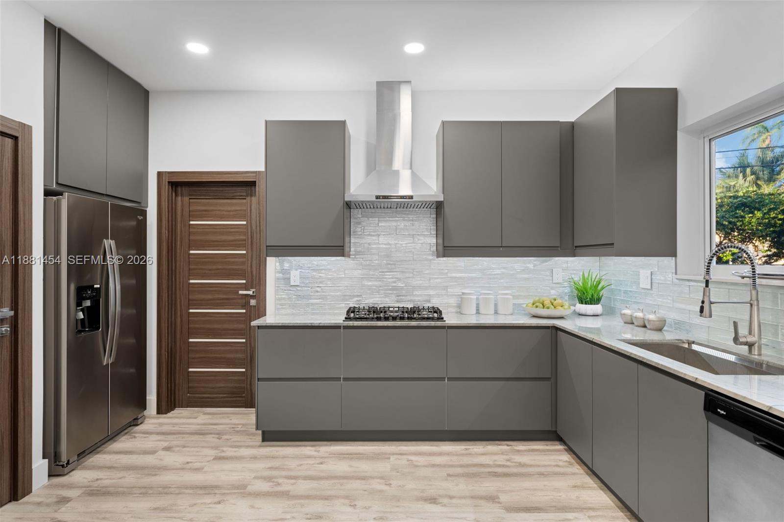 A modern kitchen features gray flat-panel cabinets, a stainless steel range hood, and light flooring — 1155 Tyler St, Hollywood FL 33019, HOLLYWOOD, FL