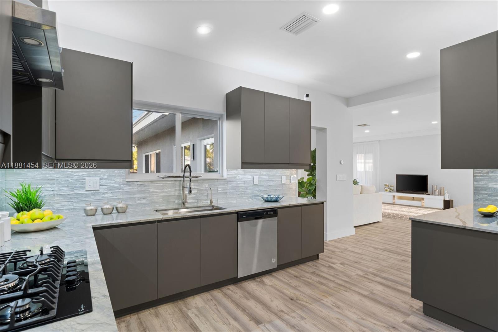 A modern kitchen features dark gray cabinetry, light stone countertops, and a stainless steel dishwasher — 1155 Tyler St, Hollywood FL 33019, HOLLYWOOD, FL
