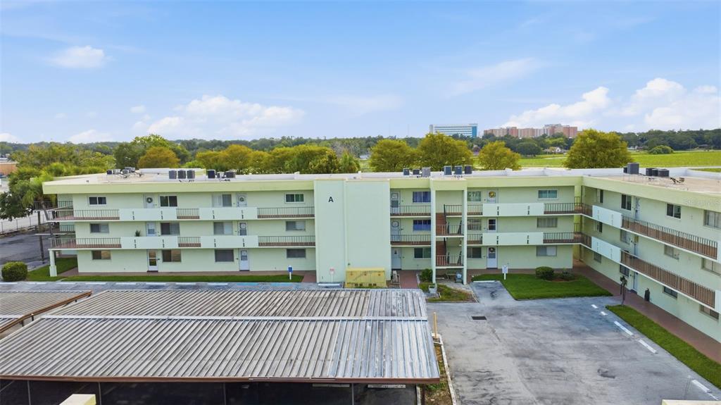 An exterior view of a three-story light green apartment building with a covered parking area — 1130 N LAKE PARKER AVENUE UNIT A205, LAKELAND, FL