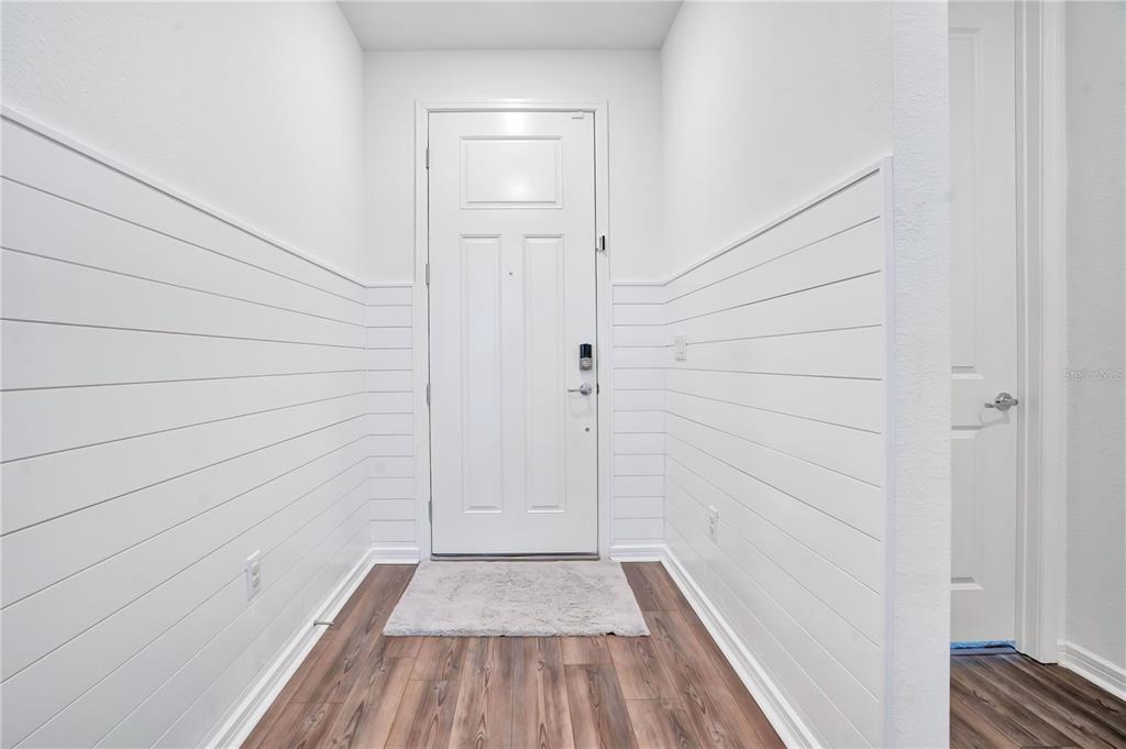 An entryway features white shiplap walls, wood-look flooring, and a central front door — 11237 ROLLING FORK TRAIL, PARRISH, FL