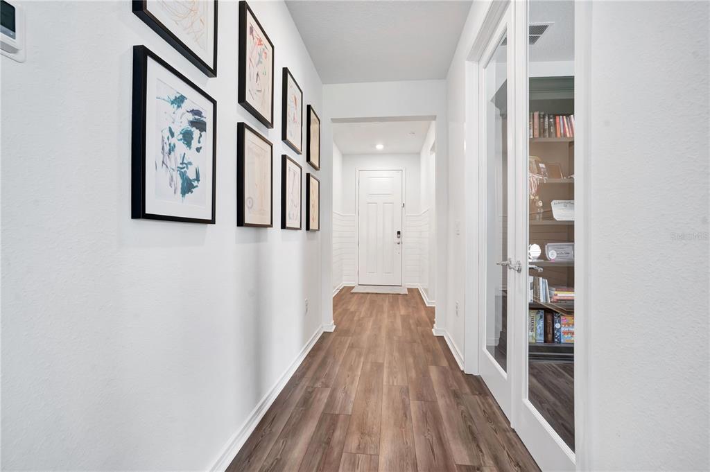 A hallway with wood-look flooring, a gallery wall of framed art, and glass-paneled double doors — 11237 ROLLING FORK TRAIL, PARRISH, FL