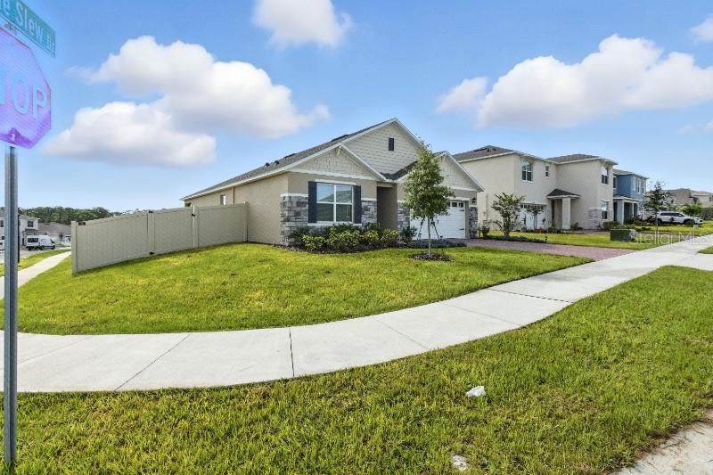 A tan suburban house with a stone facade and a vinyl fence sits on a corner — 33504 COPPER HILL WAY, SORRENTO, FL