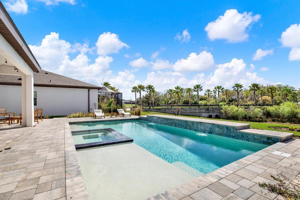 A backyard swimming pool with a spa and stone patio under a blue sky — 13113 WILDFLOWER MEADOW DRIVE, RIVERVIEW, FL