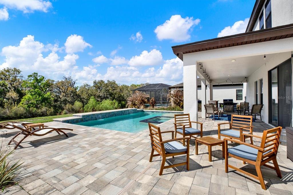 A patio with wooden chairs and a table overlooks a swimming pool and wooded area — 13113 WILDFLOWER MEADOW DRIVE, RIVERVIEW, FL