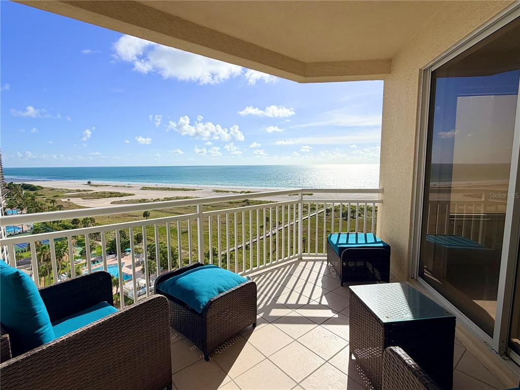 A balcony with wicker furniture overlooks a sandy beach and the ocean — 1200 GULF BOULEVARD UNIT 1001, CLEARWATER, FL