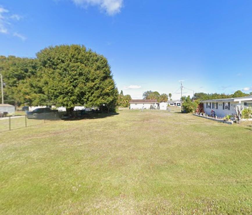 A wide, grassy vacant lot sits between a large tree and a neighboring residential house — 26510 BROOKS ROAD, PUNTA GORDA, FL